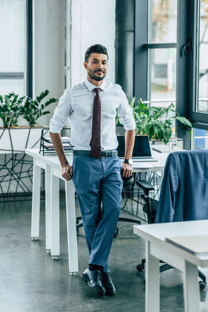young confident businessman standing near desk and looking at camera - Photo, Image