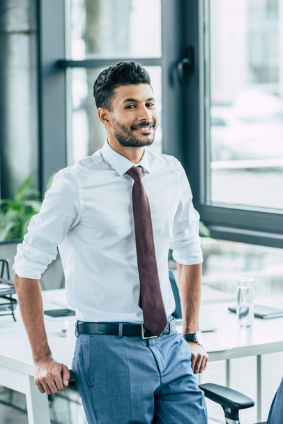 smiling businessman standing near desk and looking at camera - Fotoğraf, Görsel