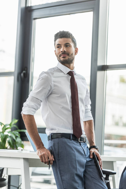 young, confident businessman looking away while standing at workplace - Valokuva, kuva