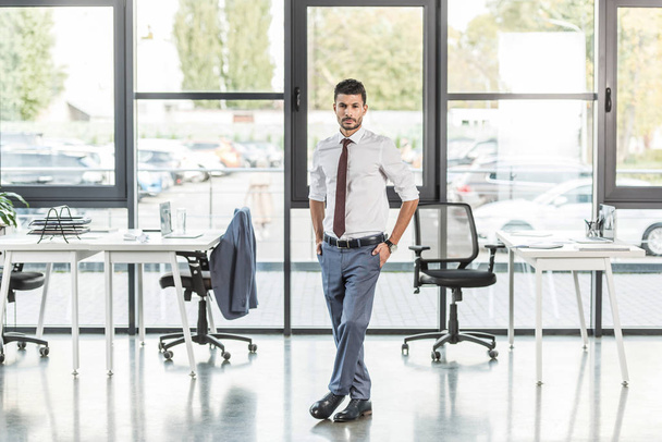 young, confident businessman standing in modern office and looking at camera  - Фото, зображення