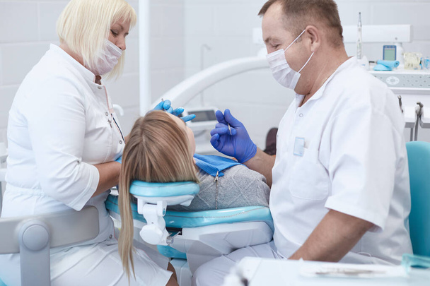 歯医者は美しい少女患者の歯を治療する。歯医者の受付の女の子。歯医者は歯を治療する - 写真・画像