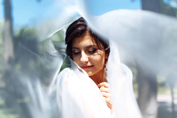 A beautiful portrait of the bride under a veil. Elegant woman with professional make up and hair style. A photo of delicate bride's hands hidden under a veil. Wedding day. Marriage. Fashion bride. - Photo, Image