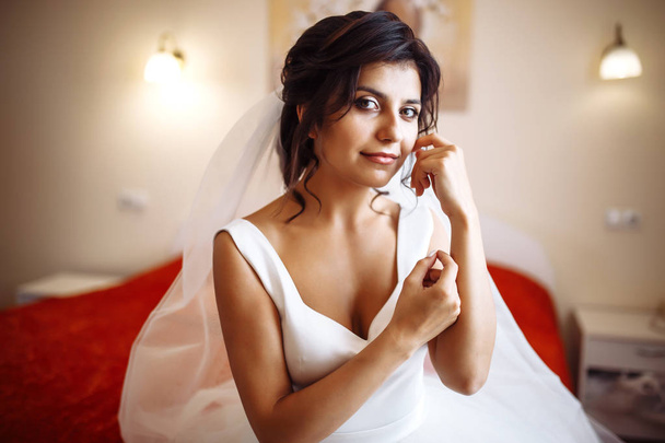 Morning of the bride. Beautiful smiling brunette bride in a white dress with a wedding bouquet in her hands. Elegant woman with professional make up and hair style. Wedding morning of the bride.  - Foto, immagini