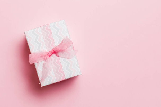 wrapped Christmas or other holiday handmade present in paper with pink ribbon on pink background. Present box, decoration of gift on colored table, top view with copy space - Photo, image