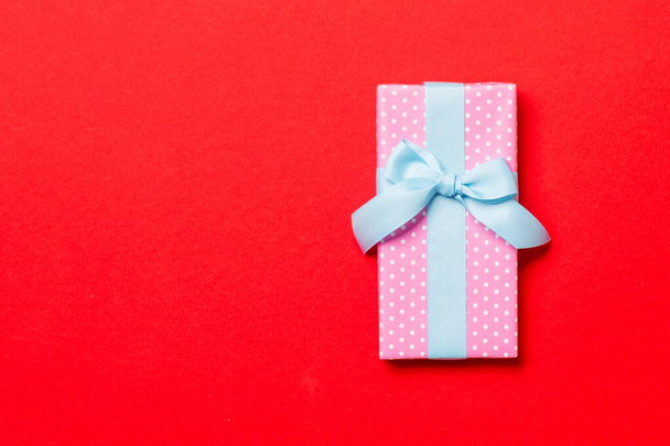 wrapped Christmas or other holiday handmade present in paper with blue ribbon on red background. Present box, decoration of gift on colored table, top view with copy space - Foto, imagen