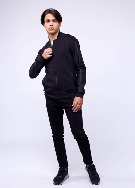 Young man in jeans, black bomber jacket on white background. - 写真・画像