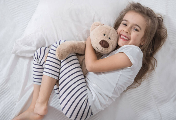 Милая маленькая девочка в постели с мягкой игрушкой
. - Фото, изображение