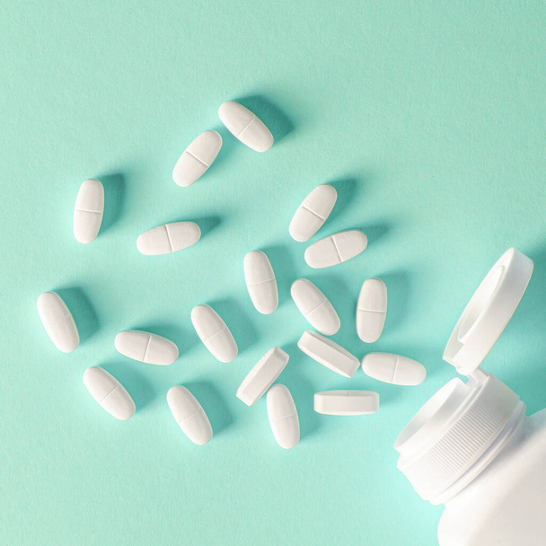 ein weißer Plastikbehälter mit weißen Tabletten liegt auf buntem Hintergrund neben weißen Tabletten - Foto, Bild