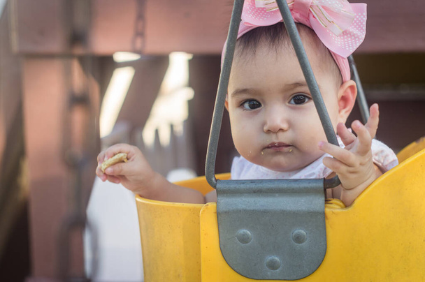 Bebé de un año, columpio amarillo y lazo rosa
 - Foto, Imagen