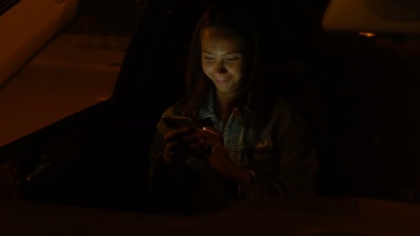 Young woman using mobile phone while sitting in a car at night - Filmati, video