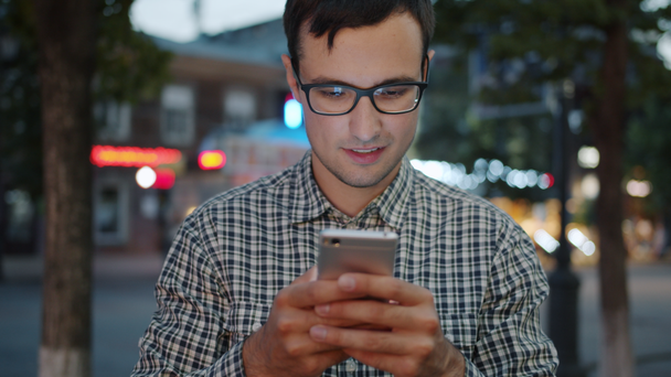 Chico guapo usando la pantalla táctil del teléfono inteligente en la calle de la ciudad por la noche
 - Metraje, vídeo