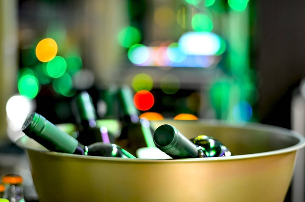 Botellas de vino sin abrir en un tazón de hierro dorado en un evento sobre un fondo desenfocado con luces multicolores
. - Foto, Imagen