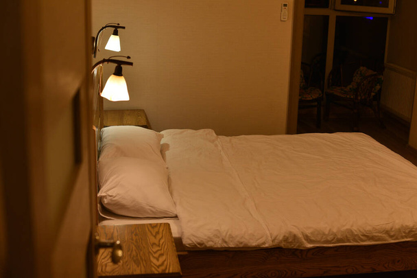 Bed in a hotel room. Bed and pillows. A bed with a wooden headboard and two cabinets and floor lamps. - Fotó, kép