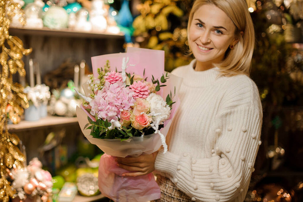 Smiling woman holding a bouquet rose color flowers with green leaves and pink cones - Photo, Image