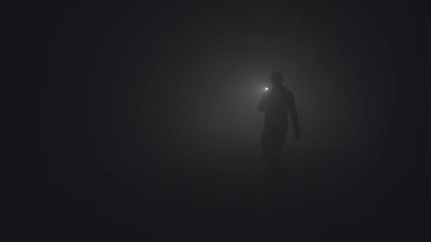 Silueta de hombre en espesa niebla. Imágenes de archivo. Silueta negra de hombre con linterna que brilla en espeso humo gris. Hombre con linterna hace su camino a través de la oscuridad en el humo
 - Metraje, vídeo