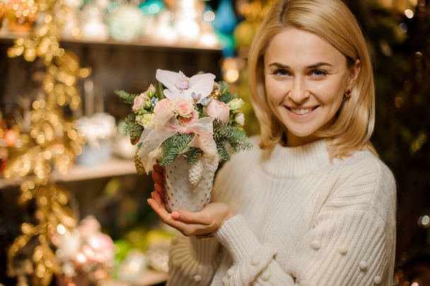 Smiling woman holding a vase with fir-tree branches, creamy roses, orchid and cone toys - Foto, Imagen