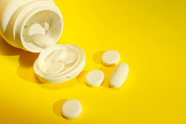 Roztroušené pilulky na žlutém pozadí. Bílá láhev a bílé pilulky na žlutém pozadí. Zdravotní a medicínský koncept. - Fotografie, Obrázek