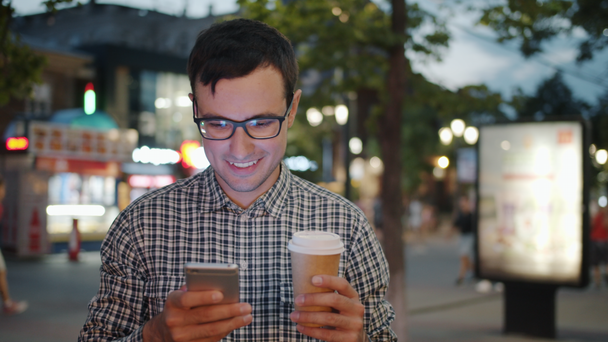 Iloinen liikemies käyttää älypuhelinta tilalla mennä kahville kadulla illalla
 - Materiaali, video