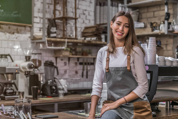 Female coffee shop owner sitting on the counter and smiling in camera - Foto, Imagen