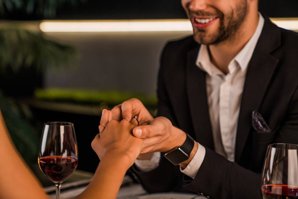 Cropped image of man putting engagement ring on woman's finger during romantic dinner - Fotografie, Obrázek