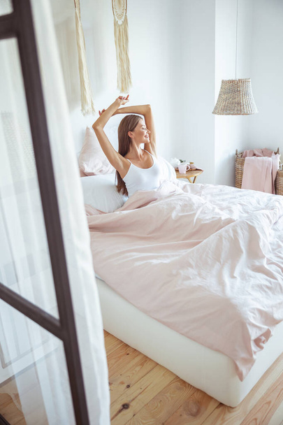 Веселая молодая женщина сидит на кровати
 - Фото, изображение