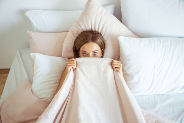 Cheerful brunette girl hiding her face under blanket - Фото, изображение