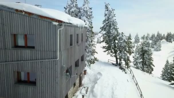 A grey wooden mountain cabin. There is snow on the roof and in the area. Aerial shot. It's winter time. - Footage, Video
