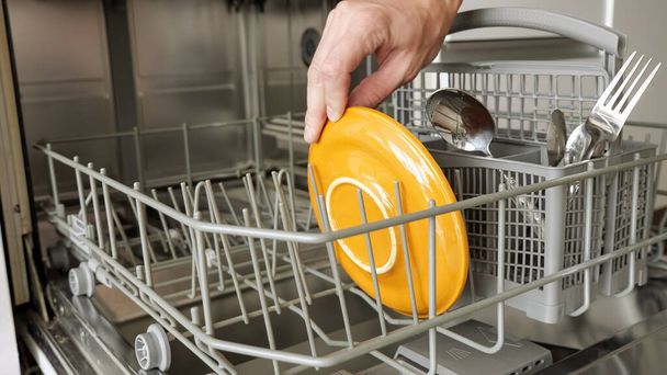 Do myčky nádobí si člověk klade špinavé talíře a příbory - Fotografie, Obrázek