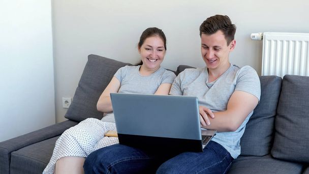 Mężczyzna i kobieta oglądają film komediowy na laptopie i śmiejąc się siedzi na kanapie. - Zdjęcie, obraz