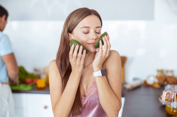 Charming young woman smelling aroma of fresh avocado - Foto, afbeelding
