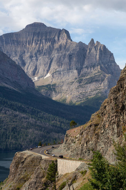 Hermosa vista de la carretera escénica con el paisaje rocoso americano de la montaña en el fondo durante una mañana nublada del verano. Tomado en Glacier National Park, Montana, Estados Unidos
. - Foto, Imagen
