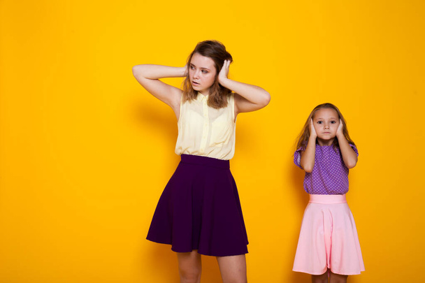 portrait of two beautiful fashionable sisters of different ages on a yellow background - Photo, Image