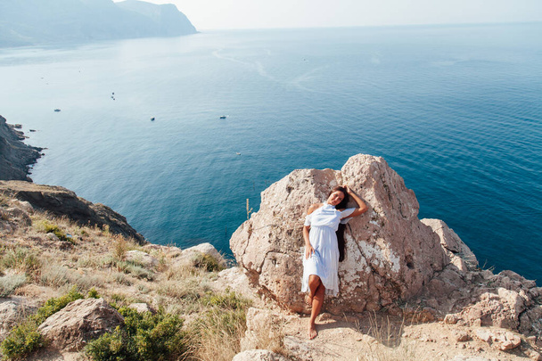 muotokuva kauniista naisesta, jolla on pitkät hiukset mekko kalliolla kalliolla meren rannalla
 - Valokuva, kuva