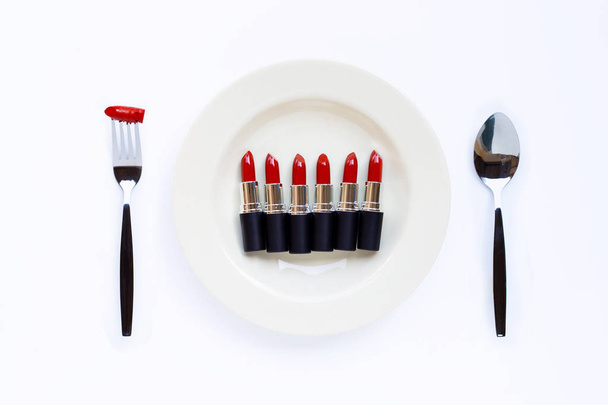Lápiz labial sobre plato blanco con tenedor y cuchara sobre blanco
  - Foto, imagen