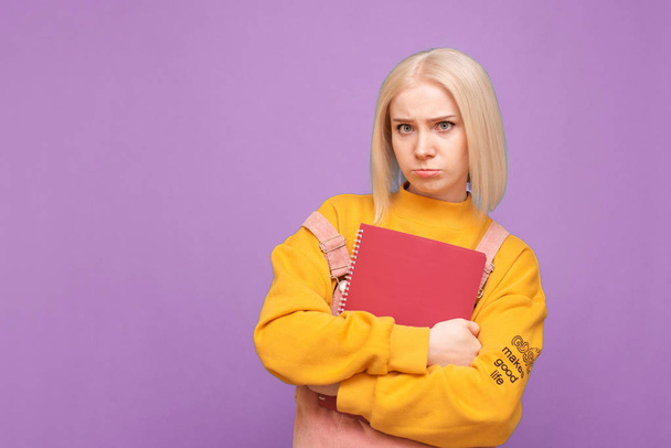 Portrait of a girl's funny student stands on a purple background, keeps books and books in her hands and looks sadly in the camera.Disappointed teenage girl poses on the camera with books in his hands - Valokuva, kuva