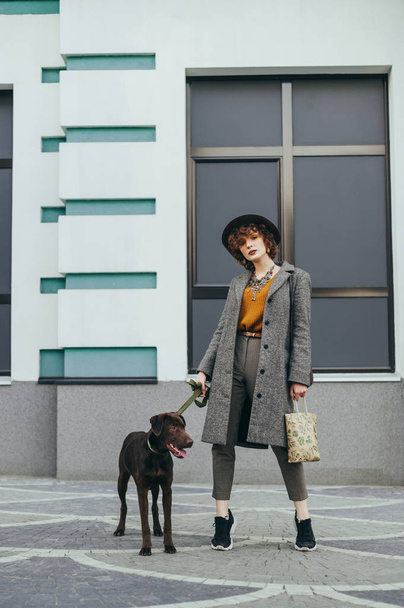 Fashionable portrait of a beautiful girl with a dog standing aga - Foto, Bild
