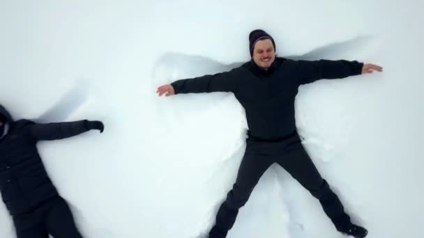 Mies hymyilee tehdessään lumienkeleitä lumeen. Hänellä ja hänen ystävillään on hauskaa ulkona.
. - Materiaali, video