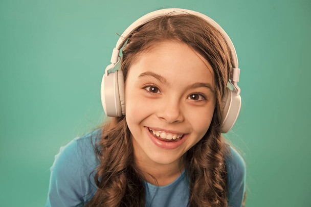 Happy songs to make you smile. Happy small girl listening to music on blue background. Little child enjoying song playing in headphones with smile on happy face. Happy fun and upbeat - 写真・画像