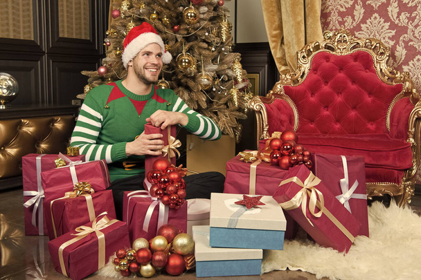 You only get this at Christmas. Delivery Christmas gifts. Guy is celebrating Christmas at home. Man in santa hat hold Christmas presents. Happy man with xmas gift boxes. The season to be jolly - Photo, Image