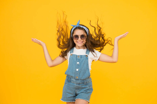 Getting your hairstyle to last all day. Happy child with curly hairstyle flying on yellow background. Small cute girl smiling with long wavy hairstyle. Fashion look of hairstyle with glamorous curls - Photo, Image