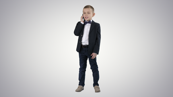 Akıllı telefonuyla konuşan sevimli küçük bir çocuk ve değişken arka planda koyu bir takım elbise içinde duruyor.. - Video, Çekim