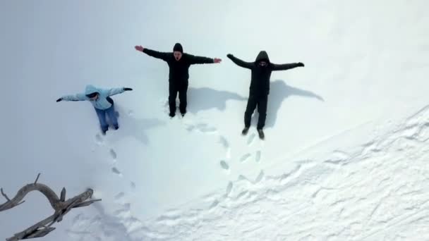 Drie mensen gooien zichzelf in de sneeuw en maken sneeuwengelen. Luchtfoto. - Video