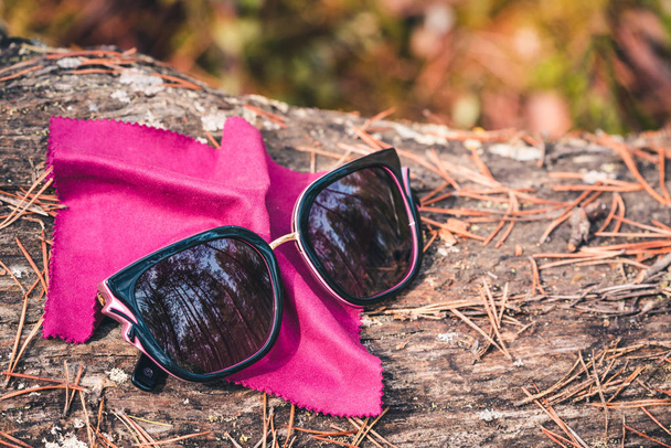 Womens sunglasses with dark lenses on burgundy shawl depicting nose in the forest on pine tree with needles. - Photo, Image