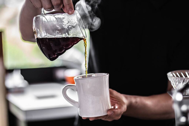 Un primer plano de una persona vertiendo café caliente en una taza
 - Foto, Imagen