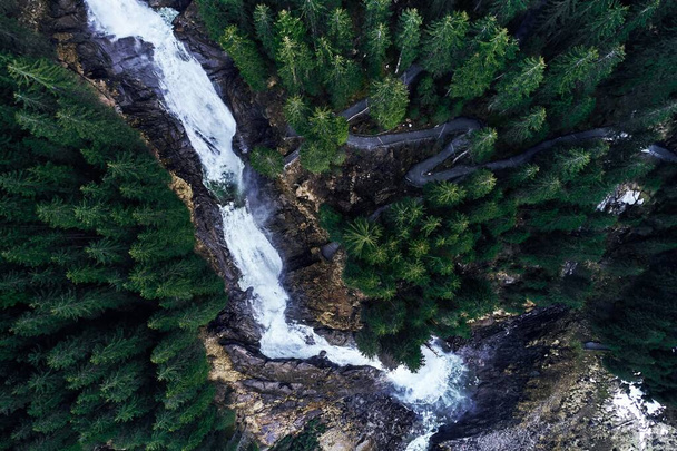 A breathtaking high angle shot of a waterfall on a rock surrounded by a forest of beautiful tall spruces - Foto, afbeelding