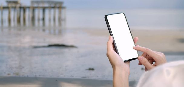 Young female holding blank screen smartphone with beach background  - Fotografie, Obrázek