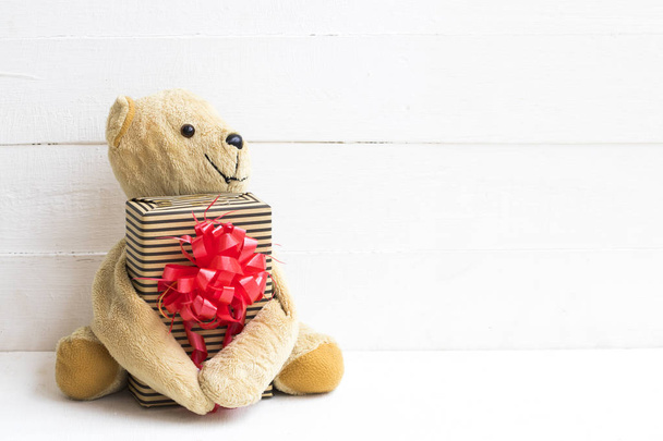 αρκουδάκι κρατώντας κουτί δώρου για τα Χριστούγεννα φεστιβάλ, το νέο έτος και ειδική διακόσμηση ημέρα στυλ καρτ ποστάλ σε φόντο λευκό ξύλινο - Φωτογραφία, εικόνα