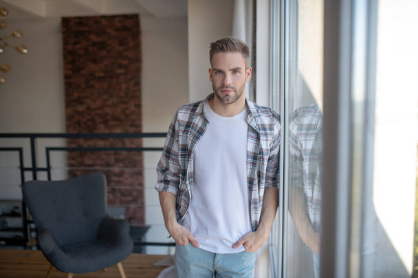 Stylish man wearing checked shirt standing near window - Foto, afbeelding