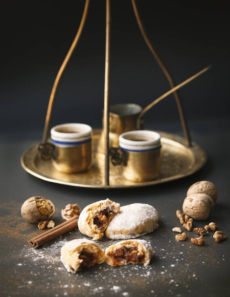 A vertical shot of golden coffee cups and a jazzve with cookies and walnuts on a black surface - Zdjęcie, obraz