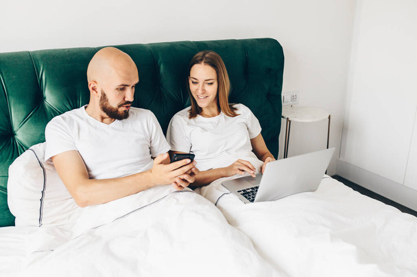 young couple lie in bed with phones. Communication and relationship problems. - Fotografie, Obrázek